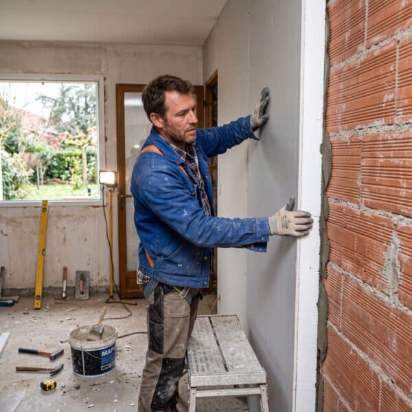 Artisan posant un panneau de doublage isolant collé sur un mur en briques lors d'un chantier de rénovation énergétique à Toulouse.